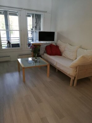 A room with a sofa, a coffee table, a flat-screen TV, and a window with blinds.