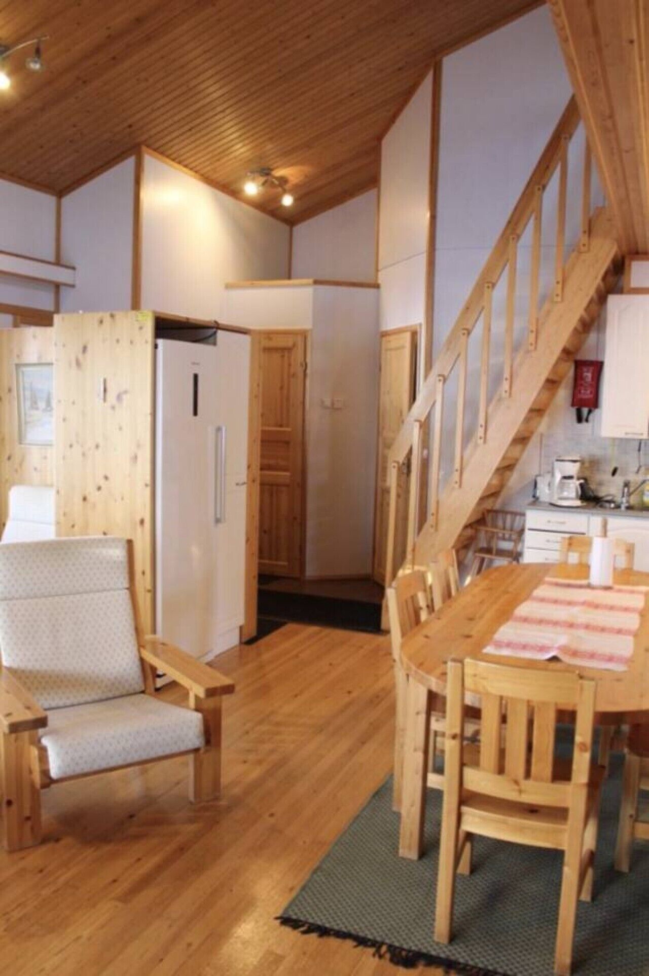 A wooden interior with a dining table, chairs, a staircase, and a kitchen area.