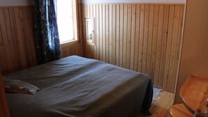 Una habitación con cama, ventana con cortinas, paredes de madera y una silla.