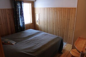A room with a bed, a window with curtains, wooden walls, and a chair. - Kivanta F 27 | Ruka Lakeside Chalet for 10 | Sauna (Ruka)