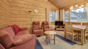 En mysig inredning med träpanel, en soffa, stolar, ett matbord och en tv.
