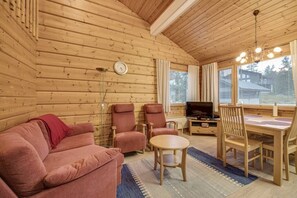 Ein gemütlicher Holzraum mit einer Couch, Stühlen, einem Esstisch und einem Fernseher.