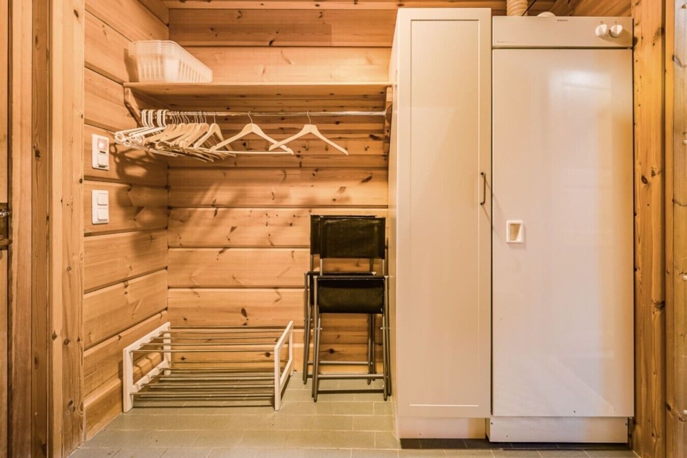 A compact room with a wooden interior, a white refrigerator, a small table, and a drying rack with clothes.