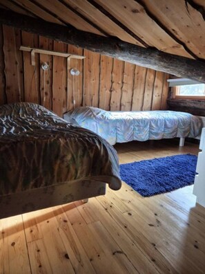 A wooden cabin with two beds, a blue rug, and a window. - Kieruka C | Cozy Log Cabin | Sauna & Fireplace (Ruka)