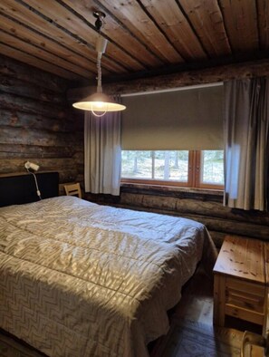 A wooden cabin room with a bed, a desk, and a window with curtains. - Kieruka C | Cozy Log Cabin | Sauna & Fireplace (Ruka)