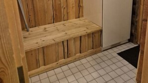 Een kleine kamer met een houten bankje, een witte kast en een witte koelkast.