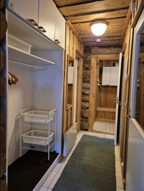 A narrow hallway with wooden walls, a tiled floor, and a ceiling with exposed beams. There is a white door on the right and a white cabinet on the left. - Kieruka C | Cozy Log Cabin | Sauna & Fireplace (Ruka)
