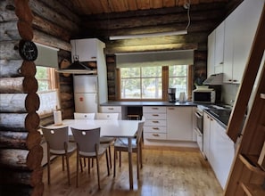A log cabin interior with a dining area, kitchen, and a large window. - Kieruka C | Cozy Log Cabin | Sauna & Fireplace (Ruka)