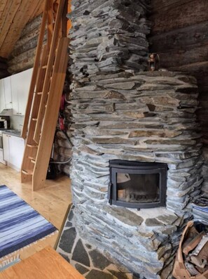 A stone fireplace with a ladder leaning against it, a wooden floor, and a blue striped rug. - Kieruka C | Cozy Log Cabin | Sauna & Fireplace (Ruka)