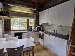 Open-plan kitchen with an electric stove, microwave and coffee maker, and a dining table with chairs. - Kieruka C | Cozy Log Cabin | Sauna & Fireplace (Ruka)