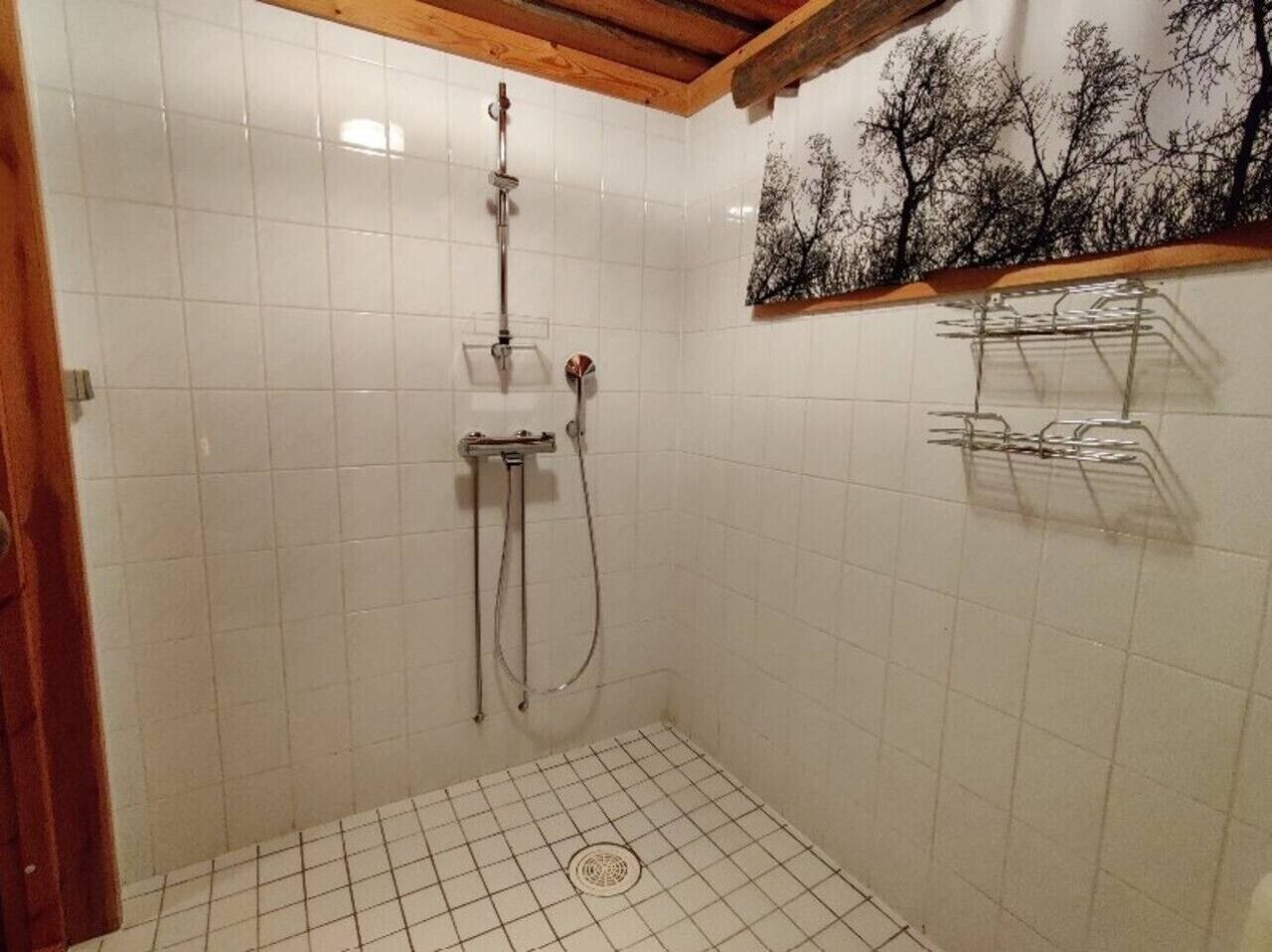 A small, tiled shower room with a wooden ceiling and a wall-mounted towel rack.