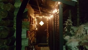 A stone-walled corridor with a door illuminated by string lights, leading to a snow-covered outdoor area. - Höperö | Charming 1BR Apt | Sauna & Fireplace (Ruka)