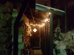 A stone-walled corridor with a door illuminated by string lights, leading to a snow-covered outdoor area. - Höperö | Charming 1BR Apt | Sauna & Fireplace (Ruka)