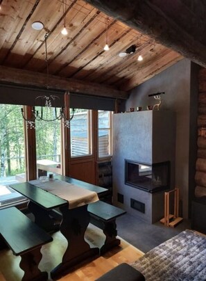 A rustic interior with a wooden ceiling, a fireplace, a dining table, and large windows.