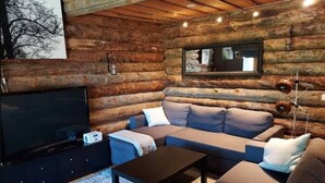 A log cabin interior with a sofa set, a television, and a lamp. - Höperö | Charming 1BR Apt | Sauna & Fireplace (Ruka)