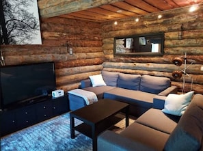 A log cabin interior with a sofa set, a television, and a lamp. - Höperö | Charming 1BR Apt | Sauna & Fireplace (Ruka)