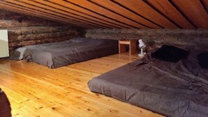 An attic room with wooden beams, two dark-colored sofas, a small wooden table, and a lamp. - Höperö | Charming 1BR Apt | Sauna & Fireplace (Ruka)