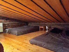 An attic room with wooden beams, two dark-colored sofas, a small wooden table, and a lamp. - Höperö | Charming 1BR Apt | Sauna & Fireplace (Ruka)
