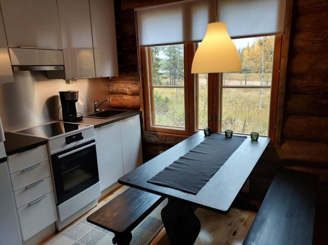 A compact kitchen with modern appliances, a dining table with benches, and a window with a view of the outdoors.