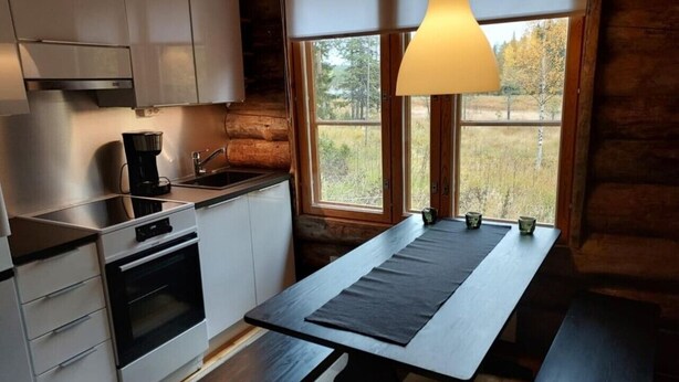 A compact kitchen with modern appliances, a dining table with benches, and a window with a view of the outdoors. - Höperö | Charming 1BR Apt | Sauna & Fireplace (Ruka)