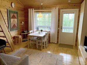A wooden interior with a dining table, chairs, a clock, a lamp, and a television. - Mestarikämpät B 9 | Cozy Lakeside Cottage & Sauna (Ruka)