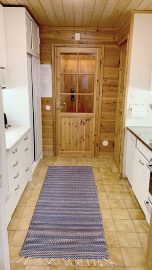 A narrow hallway with a wooden door, a small rug, and white cabinetry on either side. - Mestarikämpät B 9 | Cozy Lakeside Cottage & Sauna (Ruka)