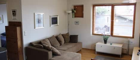 A living room with a sofa, a dining table, and a window with blinds.