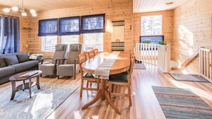 A cozy cabin interior with a dining area, seating, and a view of the outdoors. - Jyrkkälä B | Family-Friendly Apt Near Ski Slopes (Ruka)