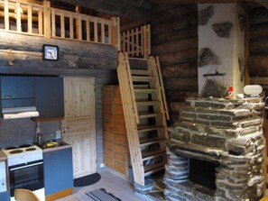 A rustic kitchen with a stone fireplace, wooden ladder, and a clock on the wall.