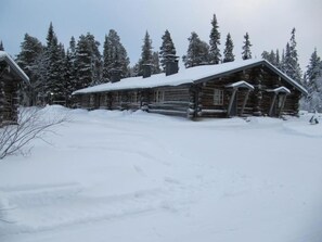 A log cabin with a snow-covered roof, surrounded by snow-laden trees. - Rukanpovi RP 7 | Cozy 1BR Cabin in Ruka (Ruka)