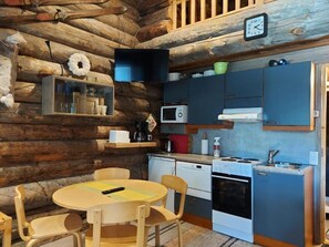 A compact kitchen with a microwave, stove, and sink, wooden cabinets, and a dining table with chairs.