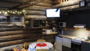 Hyggelig interiør i en hytte med et spisebord, stole, et tekøkken med komfur og et fjernsyn monteret på væggen.