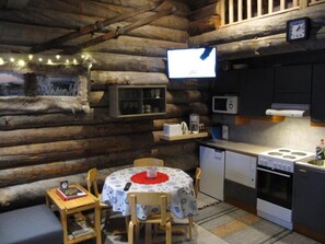 A cozy cabin interior with a dining table, chairs, a kitchen area with a stove, and a television mounted on the wall. - Rukanpovi RP 7 | Cozy 1BR Cabin in Ruka (Ruka)