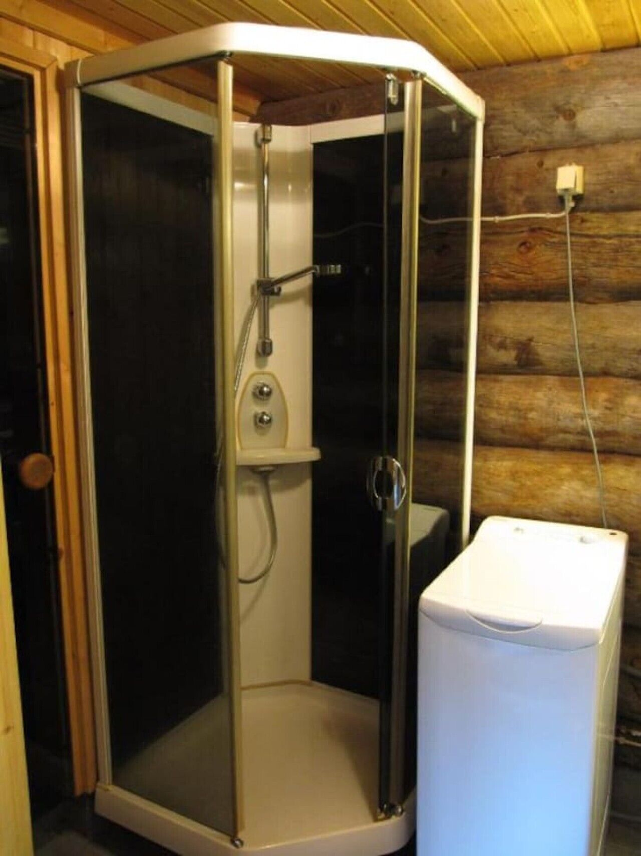 A corner shower enclosure with a glass door and a white towel dispenser beside it.