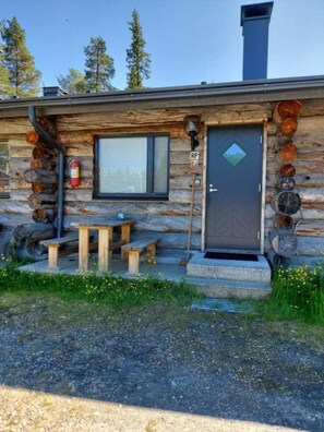 A log cabin with a wooden exterior, a window, a door with a diamond-shaped window, and a fire extinguisher mounted on the wall.