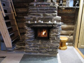 A stone fireplace with a visible fire, a wooden ladder, and a small wooden stool. - Rukanpovi RP 7 | Cozy 1BR Cabin in Ruka (Ruka)