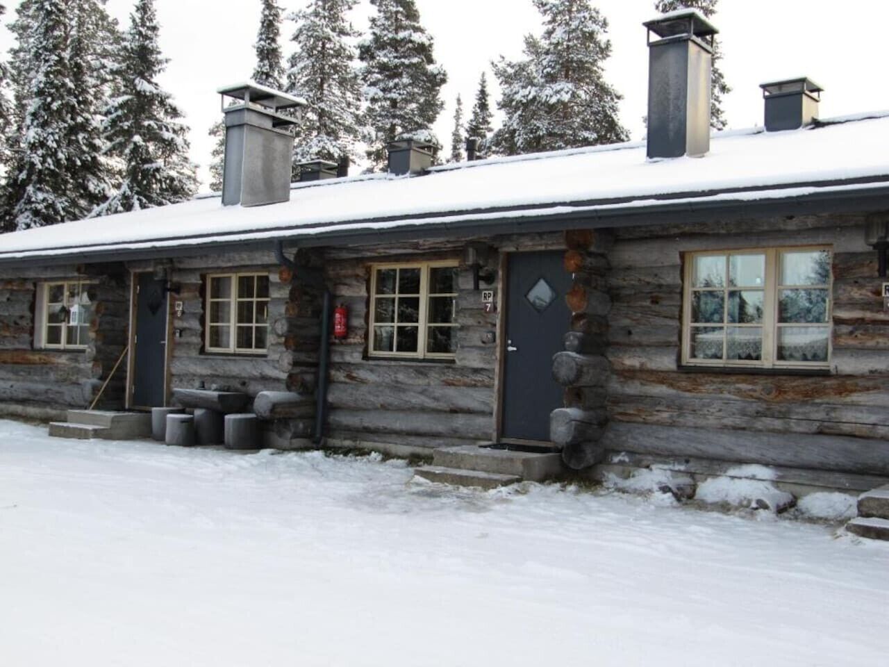 A log cabin with a snow-covered roof, a chimney, and a small porch with steps leading to the door.