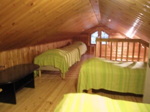 Ein Zimmer mit schrägem Dach, einem Bett mit grüner Bettdecke, einer Bank und einem Fenster.
