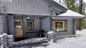 A log cabin with a wooden door and windows, surrounded by snow. - Mäntyruka B4 | Rustic Log Cabin for 6 in Ruka (Ruka)