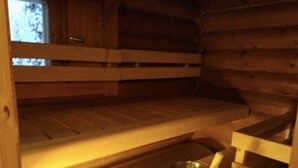 A wooden cabin interior with a bunk bed, a small table with a metal bucket, and a window with a view. - Mäntyruka B4 | Rustic Log Cabin for 6 in Ruka (Ruka)