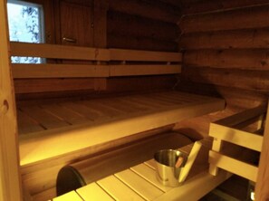 Ein Holzblockhaus-Interieur mit Etagenbett, einem kleinen Tisch und einem Metalleimer sowie einem Fenster mit Blick.