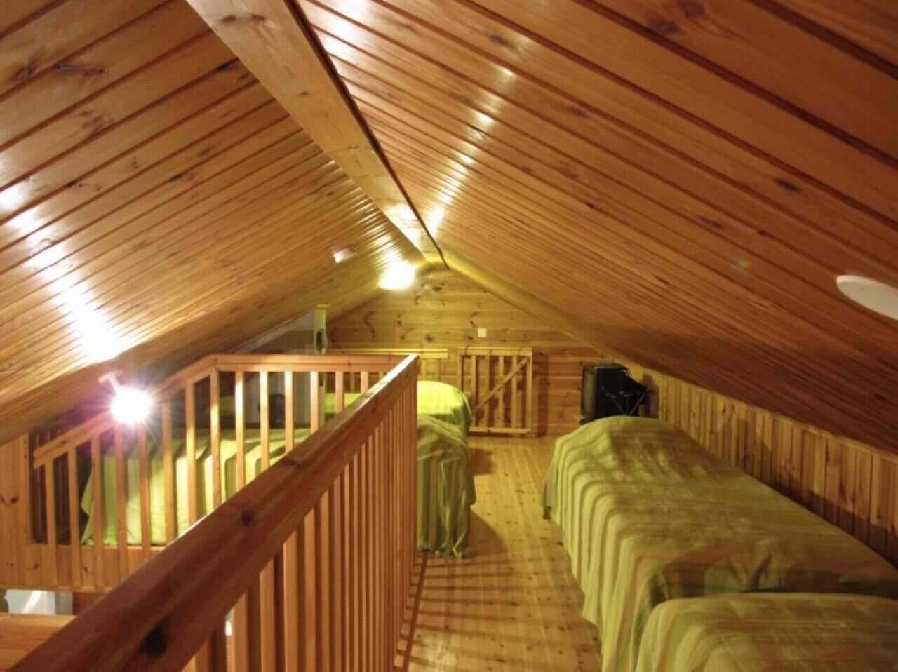 Une chambre mansardée avec de hauts plafonds, des poutres apparentes, un escalier en bois et deux lits.