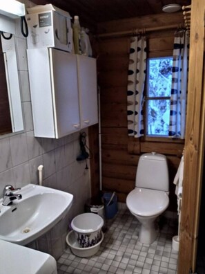 Ein kleines Badezimmer mit Waschbecken, Toilette und einem Fenster mit Vorhang.