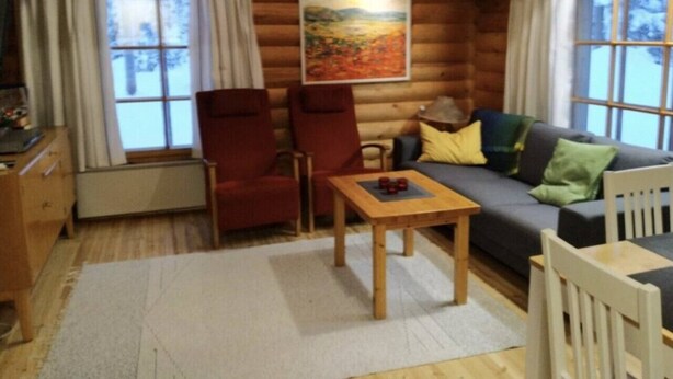 A log cabin interior with a sofa, two chairs, a small table, and a painting on the wall. - Mäntyruka B4 | Rustic Log Cabin for 6 in Ruka (Ruka)