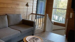 En inredning med träpanel, en soffa, ett litet runt bord, en hängande lampa och ett fönster med utsikt över träd.