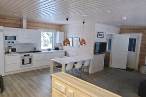 Una cocina moderna con armarios blancos, un comedor con mesa y sillas blancas, y techo de madera.