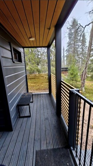 Um deck de madeira com um banco e uma mesa pequena, com vista para uma área arborizada.