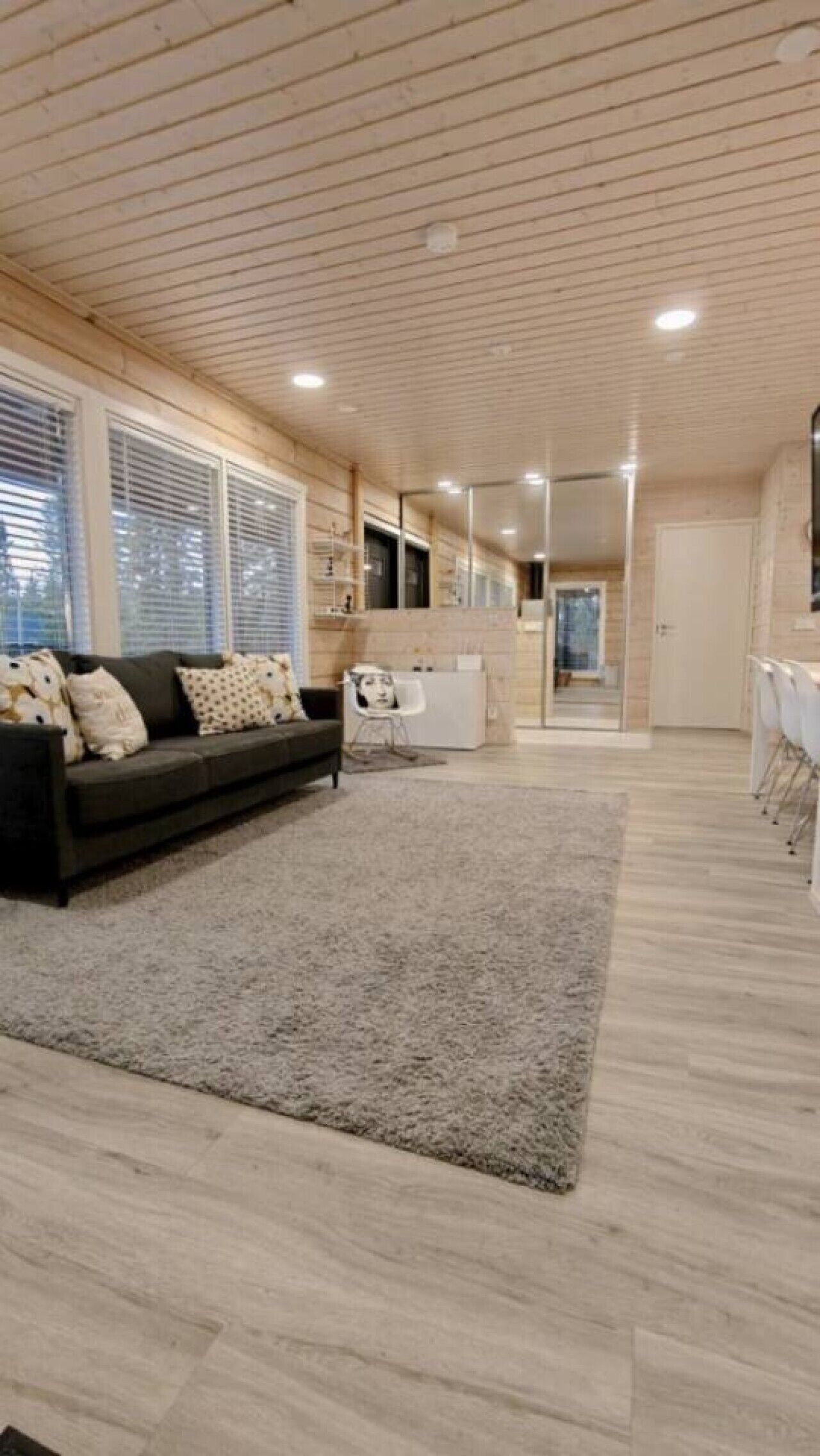 Una sala moderna con un sofá oscuro, un tapete de color claro y un techo de madera.