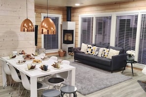 A cozy living area with a fireplace, a dining table set for a meal, and a sofa with patterned cushions. - Villa Viihy | Modern 2BR Villa Near Ski Slopes (Ruka)