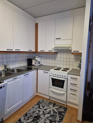 A compact kitchen with white cabinets, a stove, a sink, and a coffee maker. - Central 1BR Apt next to Ski Slopes | Ruka Centre (Ruka)